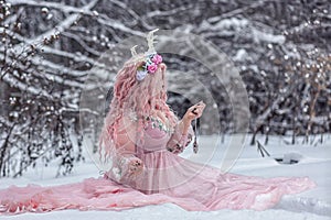 A beautiful spring fairy, a dryad with deer antlers and a crown and a light pink dress in a snowy forest.A fabulous photo. The