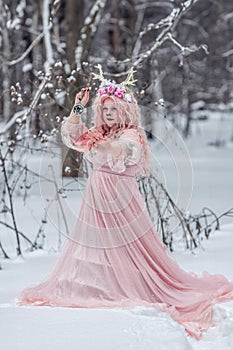 A beautiful spring fairy, a dryad with deer antlers and a crown and a light pink dress in a snowy forest.A fabulous photo. The