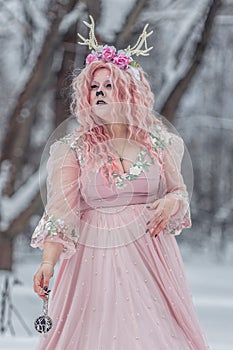 A beautiful spring fairy, a dryad with deer antlers and a crown and a light pink dress in a snowy forest.A fabulous photo. The