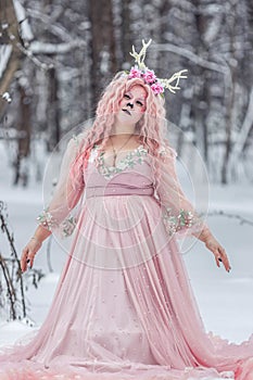 A beautiful spring fairy, a dryad with deer antlers and a crown and a light pink dress in a snowy forest.A fabulous photo. The