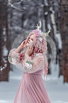 A beautiful spring fairy, a dryad with deer antlers and a crown and a light pink dress in a snowy forest.A fabulous photo. The