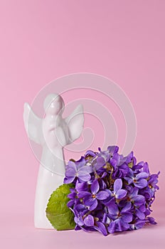 Beautiful spring flowers bouquet of violets and little white angel porcelain figurine, viola on a pink background