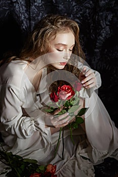 Beautiful spring girl is sitting on the floor with rose flowers in her hands. Woman in a white dress is dreaming, a romantic image