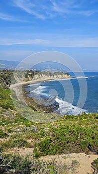 a beautiful spring landscape at Point Dume beach with blue ocean water, lush green trees and plants, homes along the cliffs, waves