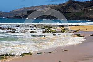 a beautiful spring landscape at Sandy Beach with blue ocean water, silky brown sand, rocks covered in green algae, palm trees