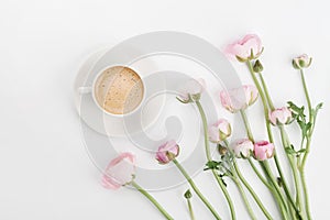 Beautiful spring Ranunculus flowers and cup of coffee on white desk from above. Greeting card. Breakfast. Pastel color. Flat lay.