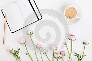 Beautiful spring Ranunculus flowers, empty notebook and cup of coffee on white desk from above. Greeting card. Breakfast. Flat lay