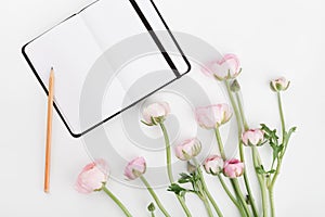 Beautiful spring Ranunculus flowers and empty notebook on white table from above. Mockup. Pastel color. Clean space for text.