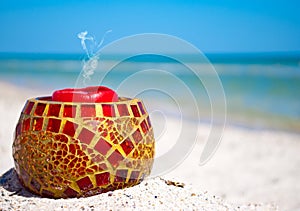 Glass candlestick and a red candle on the sand on a background of blue sea and blue sky