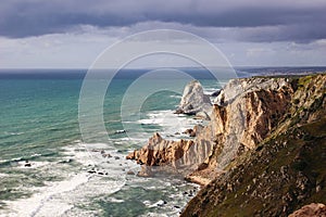 Beautiful steep coast, rocks at Praia da Ursa beach, Portugal. Dramatical sunset with stormy clouds sky at Cape Roca