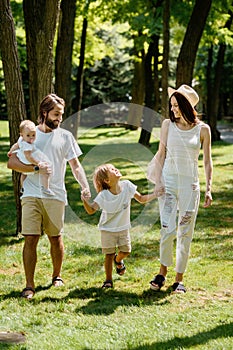 Beautiful stilish family dressed in the white clothes walks the wonderful forest on a sunny day.
