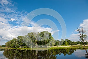 Beautiful still lake with trees on the horizon and white puffy clouds in the sky. Peaceful summer day at the cottage. Large green