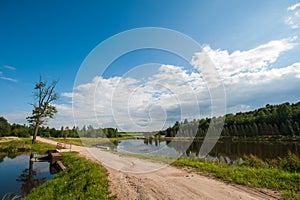 Beautiful still lake with trees on the horizon and white puffy clouds in the sky. Peaceful summer day at the cottage. Large green