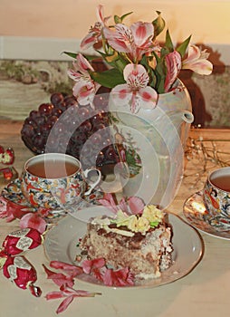 A beautiful still life consisting of a teapot with purple orchids, a transparent plate of grapes, a cake, two cups of tea, chocola
