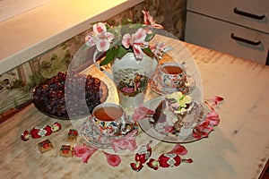 A beautiful still life consisting of a teapot with purple orchids, a transparent plate of grapes, a cake, two cups of tea, chocola