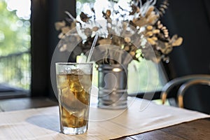 Beautiful still life with dried flowers in a tin vase and a long Island cocktail on the table by the window