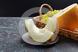 Beautiful still life with a melon on a dark background. Sliced slices on a black plate.