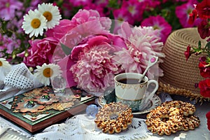 Beautiful still life with peony flowers, cup, cookies and book in the garden.