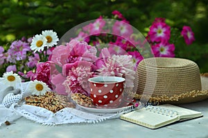 Beautiful still life with peony flowers, hat, cup and diary on the table