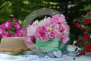Beautiful still life with peony flowers, hat and tea cup on the table.