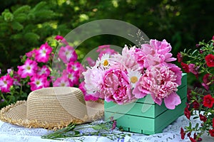 Beautiful still life with peony flowers, vintage cup and hat on the table.