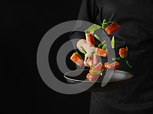 A beautiful still life of pieces of red fish, vegetables and herbs. Levitation. The cook holds in his hand a frying pan with fish