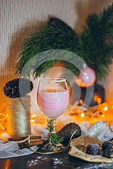 A beautiful still life scene in Christmas mood with a glass of pink beverage and sweets on the Christmas lights and fur t