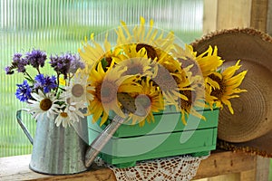 Beautiful still life with sunflowers in wooden box and wildflowers in watering can.