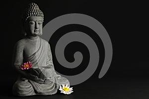 Beautiful stone Buddha sculpture with flowers on black background. Space for text