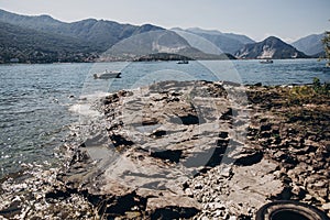 Beautiful stone shore and boats sailing to Borromean Islands on Lago Maggiore on background of sunny mountains, Stresa city, Italy