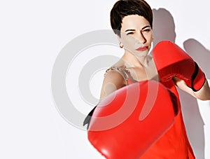 Beautiful and strong brunette woman with short hair in red dress, earrings and boxing gloves punches hits