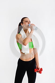 Beautiful strong happy cheerful young sports woman posing indoors drinking water with towel on neck.