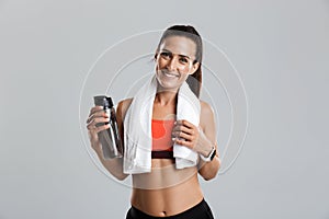 Beautiful strong happy cheerful young sports woman posing isolated indoors drinking water with towel on neck.