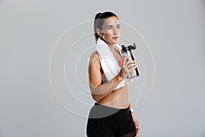 Beautiful strong happy cheerful young sports woman posing isolated indoors drinking water with towel on neck.