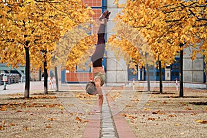 Beautiful strong sporty girl standing on hands during yoga practice on autumn city street