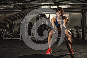 Beautiful strong sporty woman doing crossfit exercise with battle ropes