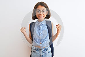 Beautiful student child girl wearing backpack and glasses over isolated white background celebrating surprised and amazed for