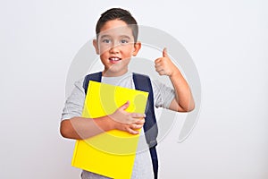 Beautiful student kid boy wearing backpack holding book over isolated white background pointing and showing with thumb up to the