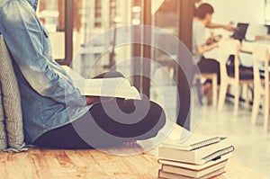 Beautiful student woman sitting at the stair and reading a book with blurred cafe workplace