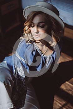 Beautiful stylish blonde girl in ethnic clothes in an embroidered shirt in a white hat in the interior in grunge style