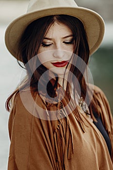 beautiful stylish boho woman with hat, fringe poncho. girl in gypsy hippie look young traveler posing near river rocks in