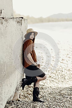 beautiful stylish boho woman with hat, leather bag, fringe poncho and boots. girl in gypsy hippie look young traveler posing near