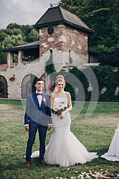 Beautiful stylish bride and groom standing in wedding aisle with rose petals on grass during matrimony, and smiling. Beautiful photo