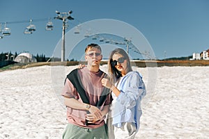 Beautiful stylish couple in casual clothes standing in the snow in the mountains while walking around the resort, posing for the