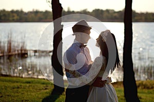 Beautiful, stylish couple hugging near the river at sunset, the bride and groom admire each other, look into the eyes