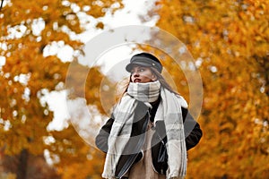 Beautiful stylish cute young woman in a brown trendy jacket in an elegant black hat with a vintage warm scarf walks in the autumn