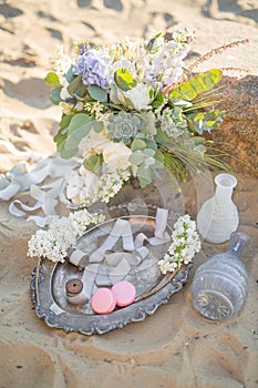 Beautiful stylish decoration with a bouquet and macaroons near the stone on the beach of a sea. Wedding design