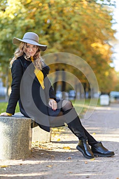 Beautiful stylish girl in autumn park on bench. fashion young woman in hat and coat in fall, outdoors