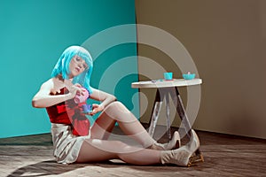 beautiful stylish girl in blue wig holding toy cup and teapot while sitting