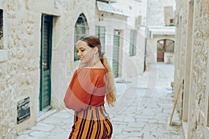 Beautiful stylish girl with long earrings, wearing an orange suit looks at the camera. Traveling around Europe Fashionable woman